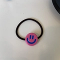Dettaglio dell'elastico per capelli in acetato rosa con ciondolo a faccina blu e cordino nero - Rosa Fucsia con Faccina Blu