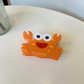 Detail view of a cute orange crab-shaped acetate hair claw clip on a white desk - Crab Claw Clip