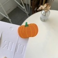 Close-up of a glossy orange pumpkin hair clip on a white decorative card display - Pumpkin