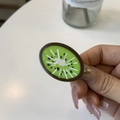 Handheld view of a vibrant kiwi fruit slice enamel hair clip with glossy green resin finish - Duckbill Hair Clips / Kiwi