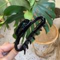 Pinza para el pelo grande de acetato negro sostenida a mano en un entorno natural - Negro