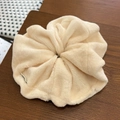 Detail view of a fluffy cream faux fur scrunchie with a textile label on dark wood - Off White