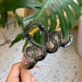 Détail d'une pince à cheveux à double vague gris foncé avec ressort en métal doré - Noir transparent
