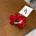 Détail d'un chouchou en velours rouge avec étiquette de marque sur surface en bois - Serre-tête Rouge en Velours avec Nœud Lettre
