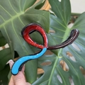 Detailed view of large tricolor wavy resin hair claw clip against a green leaf background - Blue Red Chocolate Patchwork Curved Hanger Style