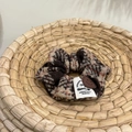 Close-up of brown plaid tweed scrunchie with smiley leather patch on woven tray - Smiley Face Patch Plaid Scrunchie