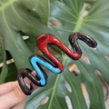 Detail of wavy colorful resin claw clip held against a green monstera leaf background - Blue Red Chocolate Patchwork Wave Style