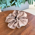 Detail view of champagne silk satin scrunchie with FMdrea label on a wooden table - Champagne