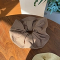 Detail view of a large ruffled checkered hair scrunchie in earth tone on a wooden table - Brown
