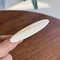 Détail d'une pince à cheveux ovale blanc crème tenue à la main sur fond de bois sombre - Pinces à cheveux bec de canard / Crème au Beurre