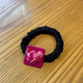 Close-up of a bear relief on a purple square base attached to a black scrunchie hair tie - Rose Pink Bear Hair Tie