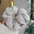 Détail d'un chouchou beige surdimensionné à plis doux avec un bouton décoratif à nœud - Blanc Grisâtre - Texture Douce