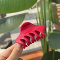 Close-up of vibrant red plastic hair claw with curved teeth held in natural sunlight - China Red