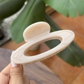 Detail of a 10cm cream beige marbled hollow hair claw clip held over a wooden table - 10cm / Light Nude Pink