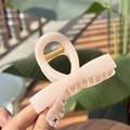 Vista dettagliata di una clip per capelli in acrilico crema tenuta a mano all'aperto - Tessuto Argilla Bianca Clip Fiocco Dritto