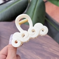 Vista macro di un fermaglio per capelli in acetato bianco panna con design a onde e ritagli - Bianco Solido