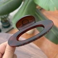 Macro shot of a tortoiseshell hollow oval hair claw clip held in hand for size display - 10cm / Matte Red Brown
