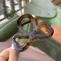 Close-up of translucent amber bow hair claw clip showing heart-shaped resin and metal spring - Glossy Light Tortoise