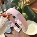 Dettaglio di un cerchietto intrecciato rosa con ciondolo a fiocco argento su tavolo in legno - Cerchietto a Quadri Rosa Crema