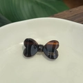 Schildpatt-Haarspange in Schleifenform aus Acetat mit goldenem Logo auf Keramikteller - Schokoladenkaffee
