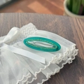 Detailed view of an oval green acrylic hair clip with rhinestones on a wood background - Transparent Lake Blue