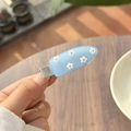 Detail van een lichtblauwe haarclip met vijf witte bloemen en gouden accenten erop - Muntblauw