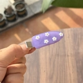 Detailopname van een lavendelkleurige haarspeld van hars met kleine witte bloemen en goud - Druivenpaars