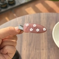 Detail van een roze hars haarklem met kleine witte bloemen op een houten achtergrond - Sandelhout