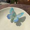 Detailed close-up of blue butterfly hair claw clip with gradient wings on white plate - Painted Blue Green Pale Pink
