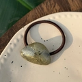 Detailansicht eines Vintage-Haargummis aus Bernstein-Harz mit goldener Handmade-Prägung - Gold Webstruktur - Goldetikett Haarseil