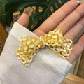 Detailed view of a yellow and white hollow bow hair clip held in hand with natural background - Yellow Dots