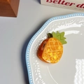 Close-up of a yellow pineapple hair claw clip with green leaves on a ceramic tray - Pineapple