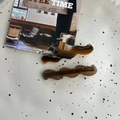 Detail von wellenförmigen Schildpatt-Haarspangen mit goldener Aufschrift auf Keramiktablett - Kaffee Schildpatt