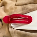Close-up of a glossy dark red hair claw clip resting on a white ceramic plate and knit sweater - China Red
