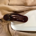 Detail of a glossy dark reddish-brown hair claw clip on a white ceramic tray background - Brown Camel