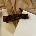 Detail einer dunkel bernsteinfarbenen Haarklammer mit Schildpattmuster auf weißem Tablett - Glänzendes Schildpatt