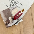 Elegant dark red acetate hair clip with gold logo on a minimalist canvas background - Red