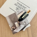 Detail of black acetate hair clip with gold logo on white fabric and wood surface - Black