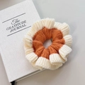 Détail d'un chouchou en maille orange et beige avec texture ondulée posé sur un livre - Blanc Lait-Orange