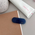 Detail showing deep blue translucent resin hair clip with gold logo in a flat lay setup - Transparent Dark Blue