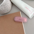 Detailed view of a pink translucent rectangular hair clip clipped onto a paper notebook - Transparent Pink