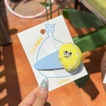 Cute lemon hair clip with yellow embroidery and light blue fabric base on display card - Sad Lemon Blue Clip