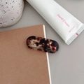 Detailed macro view of an oval acetate hair clip with tortoiseshell texture and gold lettering - Transparent Tortoiseshell