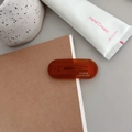 Macro detail of translucent dark brown oval hair clip with gold label text on wood desk - Transparent Dark Orange