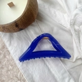 Detail of blue triangular hair claw clip with golden metal spring on white lace fabric - Klein Blue