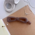 Close-up of a dark brown bow-shaped resin hair clip on a minimalist desk setting - Transparent Brown
