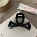 Détail d'une pince à cheveux noire brillante avec motif nœud ajouré sur socle blanc - 8.5cm / Noir Brillant