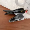 Detail of a bird-shaped hair claw clip in black and white finish on a wooden table - Black Star Swallow
