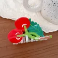 Detail view of a glossy red cherry hair claw clip with green leaves on a lace background - Cherry on Tree