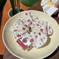 Creamy white hair scrunchie with red cherry print and decorative brand tag - Cherry Orchard Scrunchie